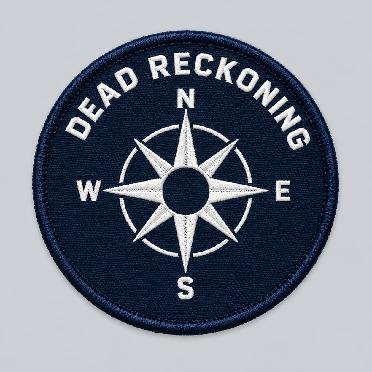 Round navy embroidered patch with a white compass rose that has no needle, under the words Dead reckoning